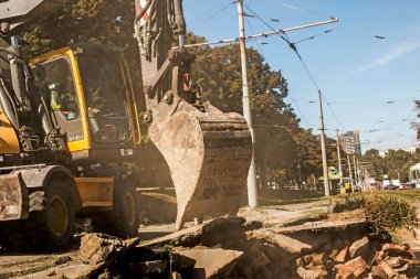 Kazıcı, greyder ve işçiler bir tren durağını söktükten sonra enkazı kaldırıyorlar. Tramvay raylarında çalışır.