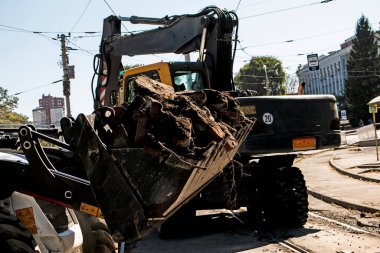 Kazıcı, greyder ve işçiler bir tren durağını söktükten sonra enkazı kaldırıyorlar. Tramvay raylarında çalışır.