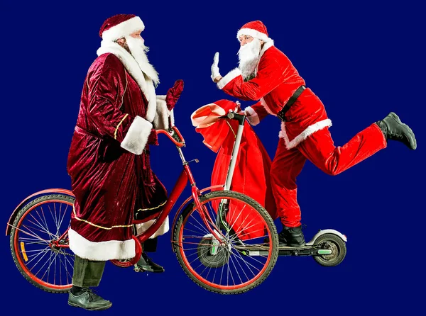 两个戴着圣诞礼帽和红色西服的快乐圣诞老人骑着一辆摩托车和一辆装有礼物袋的自行车 祝2022年新年快乐 圣诞快乐 — 图库照片