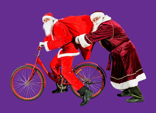两个戴着圣诞礼帽 身穿红色西服的快乐圣诞老人骑着一辆装有一袋礼物的自行车 祝2022年新年快乐 圣诞快乐 — 图库照片