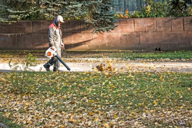 Dnepropetrovsk, Ukrayna - 10.19.2021: Yel değirmeniyle kuru yaprakları temizlemek. Bir belediye çalışanı şehir parkını temizler. Şehir parkları kışa hazırlanıyor.