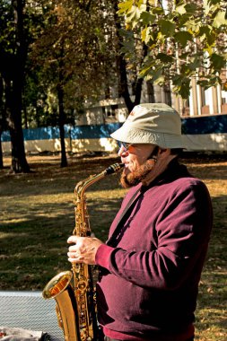 Dnepropetrovsk, Ukrayna - 09.17.2021: Parkta saksafon çalan bir adam. Saksafonlu bir sokak müzisyeni hayır işi için müzik yapıyor. Bir rüzgar enstrümanında halk solo performansı