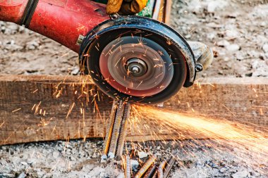 Erkek bir el, destek parçalarını öğütücü kullanarak kesiyor. İnşaat alanındaki kıvılcımlarla birleştirilmiş çelik kesme. Açı öğütücüyle metal keserken kıvılcımlar