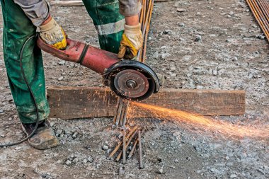 Erkek bir el, destek parçalarını öğütücü kullanarak kesiyor. İnşaat alanındaki kıvılcımlarla birleştirilmiş çelik kesme. Açı öğütücüyle metal keserken kıvılcımlar
