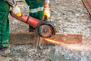 Erkek bir el, destek parçalarını öğütücü kullanarak kesiyor. İnşaat alanındaki kıvılcımlarla birleştirilmiş çelik kesme. Açı öğütücüyle metal keserken kıvılcımlar