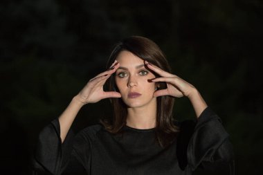 Esmer bir arka planda çekici bir genç kadının portresi. Kız bir şeye üzüldü ve elleriyle başını tuttu..