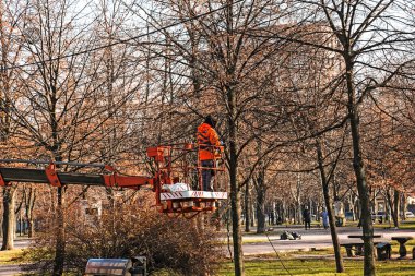Dnepropetrovsk, Ukrayna - 11.26.2021: Bir kamyon vinci üzerindeki belediye çalışanları kentin parklarındaki ağaçları Noel ışıklarıyla kurup süslediler. Yüksek irtifa çalışması.