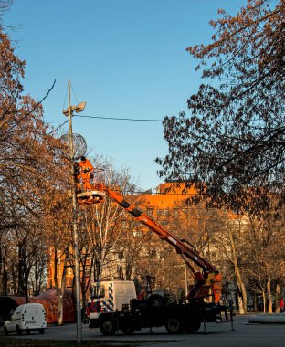 Dnepropetrovsk, Ukrayna - 11.24.2021: Kamyon vinçindeki belediye çalışanları şehrin sokaklarını Noel ışıklarıyla süslediler. Güneşli havada yüksek irtifa çalışması.