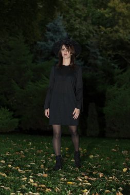 Siyah şapkalı ve büyümüş siyah elbiseli güzel bir kadın. Eski tarz modaya uygun bir kız. Büyük kenarlı siyah şapka. Cadılar Bayramı cadısı.