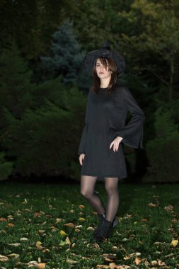 Siyah şapkalı ve büyümüş siyah elbiseli güzel bir kadın. Eski tarz modaya uygun bir kız. Büyük kenarlı siyah şapka. Cadılar Bayramı cadısı.