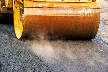 Küçük buharlı silindirler asfaltı dümdüz etmiş. Asfalt kaldırımda ağır titreşimli silindir çalışıyor. Tekerlek parçası, şehir yolu yapım aşamasında, asfaltlama devam ediyor.