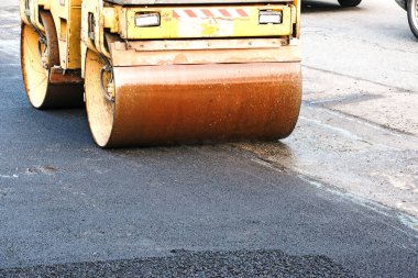 Küçük buharlı silindirler asfaltı dümdüz etmiş. Asfalt kaldırımda ağır titreşimli silindir çalışıyor. Tekerlek parçası, şehir yolu yapım aşamasında, asfaltlama devam ediyor.