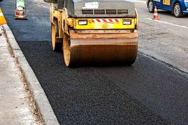 Küçük buharlı silindirler asfaltı dümdüz etmiş. Asfalt kaldırımda ağır titreşimli silindir çalışıyor. Tekerlek parçası, şehir yolu yapım aşamasında, asfaltlama devam ediyor.
