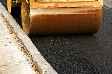 Küçük buharlı silindirler asfaltı dümdüz etmiş. Asfalt kaldırımda ağır titreşimli silindir çalışıyor. Tekerlek parçası, şehir yolu yapım aşamasında, asfaltlama devam ediyor.