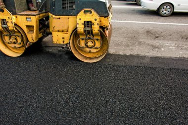Küçük buharlı silindirler asfaltı dümdüz etmiş. Asfalt kaldırımda ağır titreşimli silindir çalışıyor. Tekerlek parçası, şehir yolu yapım aşamasında, asfaltlama devam ediyor.