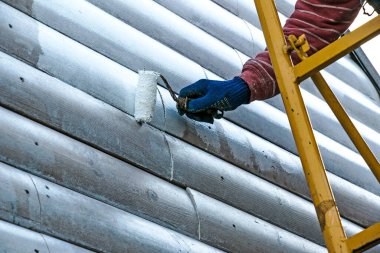 Duvarı minderle boyayan bir işçinin eli. Binanın dış duvarının boyanması, beyaz boyayla yenilenmesi. Beyaz arka planda boya silindiri tutan bir erkek.