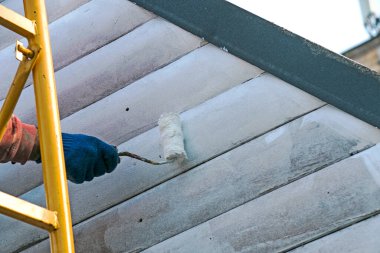 Duvarı minderle boyayan bir işçinin eli. Binanın dış duvarının boyanması, beyaz boyayla yenilenmesi. Beyaz arka planda boya silindiri tutan bir erkek.