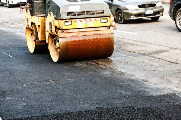 Küçük buharlı silindirler asfaltı dümdüz etmiş. Asfalt kaldırımda ağır titreşimli silindir çalışıyor. Tekerlek parçası, şehir yolu yapım aşamasında, asfaltlama devam ediyor.