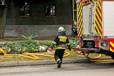 Dnepropetrovsk, Ukrayna -09.20.2021: Beş katlı bir binanın en üst katında yangın. İtfaiyeci, yangın yerine elektrikli testereyle koşar..