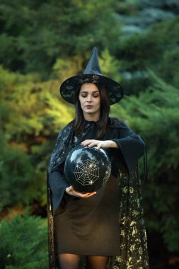 Siyah elbiseli ve pelerinli çekici bir genç kadının portresi. Siyah bir topun ellerinde. Koyu saçlı, kahverengi gözlü ve makyajlı bir kız..