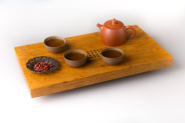Ceramic teapot and three traditional cups for oriental tea drinking on a wooden table for tea ceremonies on a white background. The cups are filled with freshly green tea and goji berries for a snack.