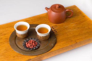 Ceramic teapot and three traditional cups for oriental tea drinking on a wooden table for tea ceremonies on a white background. The cups are filled with freshly green tea and goji berries for a snack