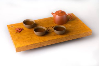 Ceramic teapot and three traditional cups for oriental tea drinking on a wooden table for tea ceremonies on a white background. The cups are filled with freshly green tea and goji berries for a snack.