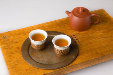Ceramic teapot and three traditional cups for oriental tea drinking on a wooden table for tea ceremonies on a white background. The cups are filled with freshly brewed green tea.