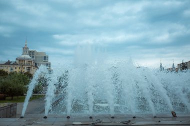 Fıskiyenin fıskiyeleri fırtınalı bir gökyüzünün arka planına çarpıyor. Bulutların ve mavi gökyüzünün arka planına karşı bir damla su. Şehir çeşmesinden püskürt..