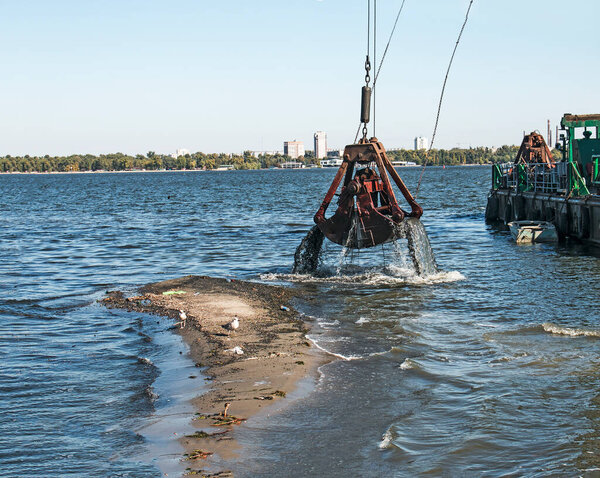 Cleaning the newly formed island from industrial waste on the Dnieper River by a dredger. Environmental problems of modern rivers. Ecology concept.