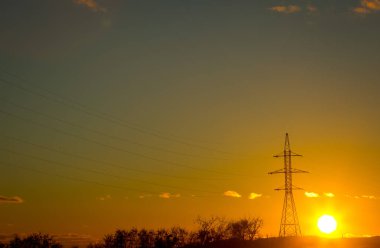 Güç iletim kuleleri veya altın gökyüzü ve bulutlu elektrik direkleri. Gün batımında elektrik hattı olan siluetli elektrik direği..