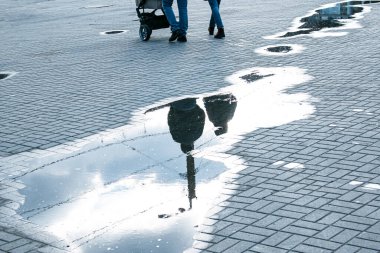 Parkta yürüyen insanlar yağmurdan sonra bir su birikintisine yansıyor. Baharın renkli resimleri.