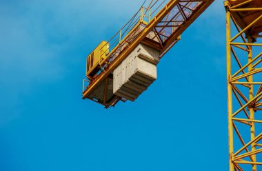 Mavi gökyüzüne karşı uzun sarı bir bumbası olan yüksek binalı bir vinç..