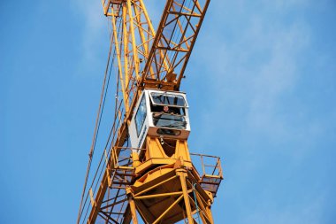 Dnepropetrovsk, Ukrayna - 11.30.2021: Mavi gökyüzüne karşı uzun sarı bir patlama ile yüksek binalı inşaat vinci. Yük kaldırırken bir marangozun duyguları.