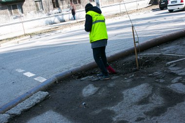 Dnepropetrovsk, Ukrayna - 03.16.2021: Sarı üniformalı bir hademe şehir caddesi boyunca kaldırımı süpürüyor. Güneşli bir bahar günü. Belediyenin kamu hizmeti.