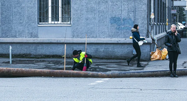 ウクライナのDnepropetrovsk 2021 黄色の制服を着た清掃員が街の通りの道路に沿って歩道を掃き掃除します 春の晴れた日 地方公共団体の業務 — ストック写真