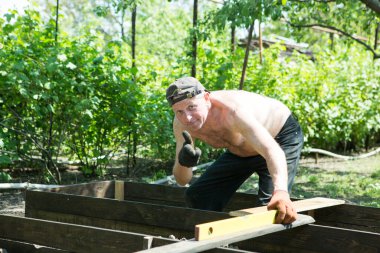 Yetişkin bir adam, kişisel bir komploda yüksek yataklar yapar. Usta, tahtaların doğru boyutlarını korumak için bir seviye aracı ile çalışır.