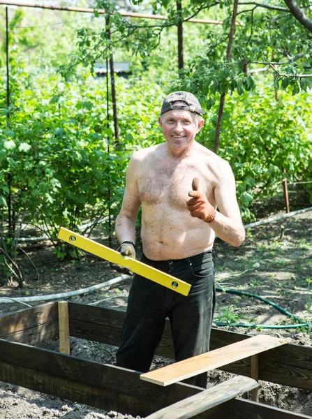 Yetişkin bir adam, kişisel bir komploda yüksek yataklar yapar. Usta, tahtaların doğru boyutlarını korumak için bir seviye aracı ile çalışır.