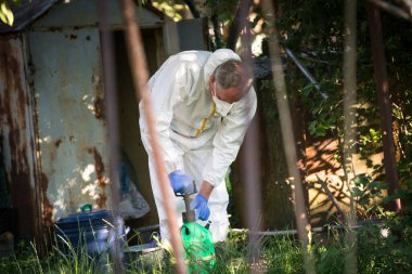 Bitkileri böcek ilacı ile tedavi etme süreci. Koruyucu kıyafetli ve maskeli bir çiftçi işe bir polen taşıyıcı hazırlar..