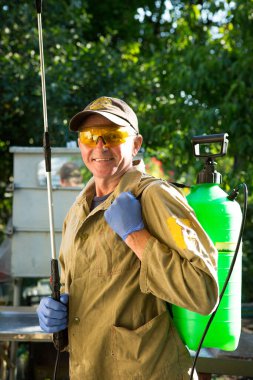 Bitkileri böcek ilacı ile tedavi etme süreci. Gözlüklü, eldivenli ve iş elbiseli bir çiftçi gülümser ve elinde bir polen taşıyıcı tutar..
