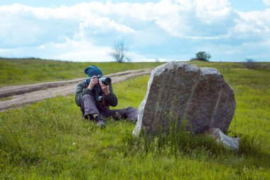 Dnipropetrovsk bölgesi, Ukrayna - 04.01.2022: Spor giyimli ve kameralı bir erkek turist tarlada büyük bir taşın yanında dinleniyor.