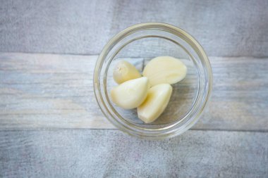 Bowl with peeled garlic cloves on gray wooden background, top view