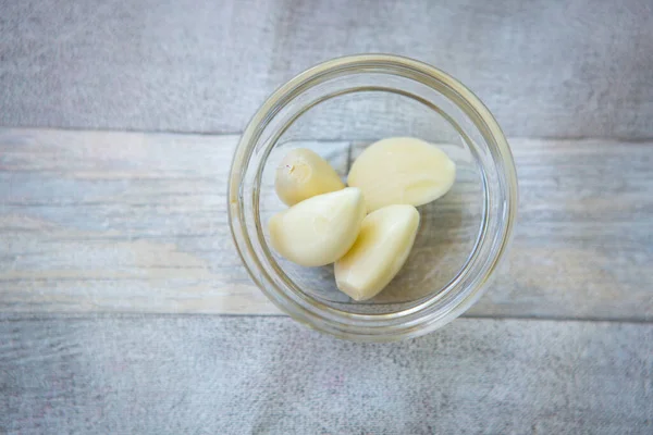 Bowl with peeled garlic cloves on gray wooden background, top view