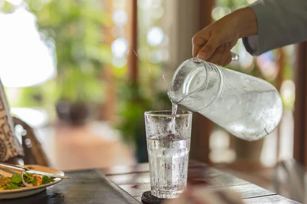 Ober hand gieten water met ijs in glazen op tafel. — Stockfoto