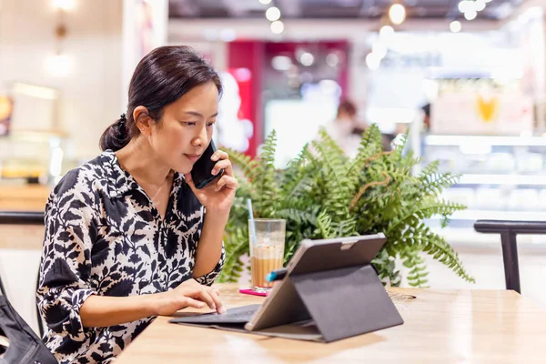 Attractive woman talking on mobile phone while working on laptop sitting in coffee shop. — Stock Photo, Image