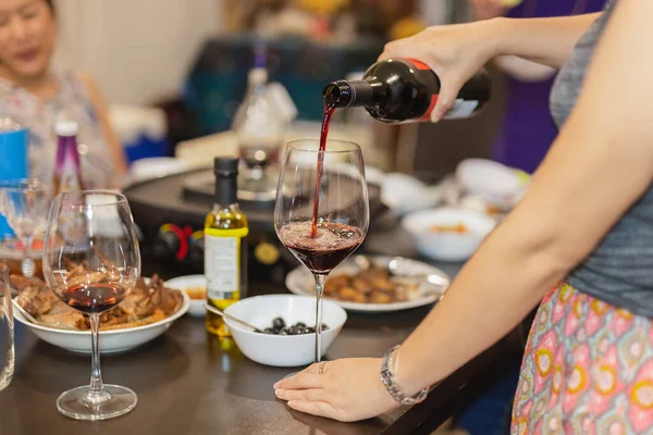Друзья-женщины празднуют дома наливая красное вино в бокалы. — стоковое фото