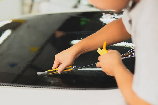 Male specialist applying window tinting film on the car and cuts off excess part with a knife. — Stock Photo, Image