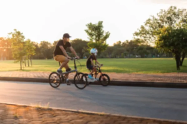 Pai e filho andando de bicicleta no parque ao pôr do sol. — Fotografia de Stock