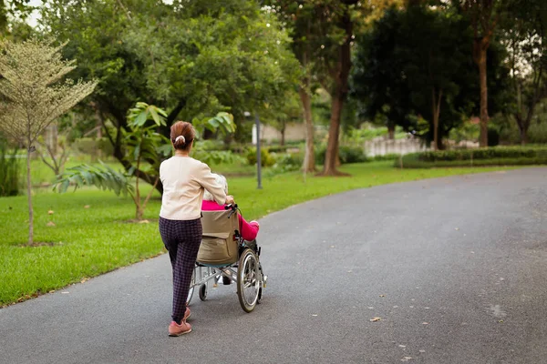 Bekçi yaşlı kadını parkta tekerlekli sandalyeye itiyor.. — Stok fotoğraf
