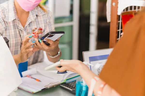 Cliente femenino en máscara protectora hace mujer de ventas de pago móvil sin contacto en tienda minorista. — Foto de Stock